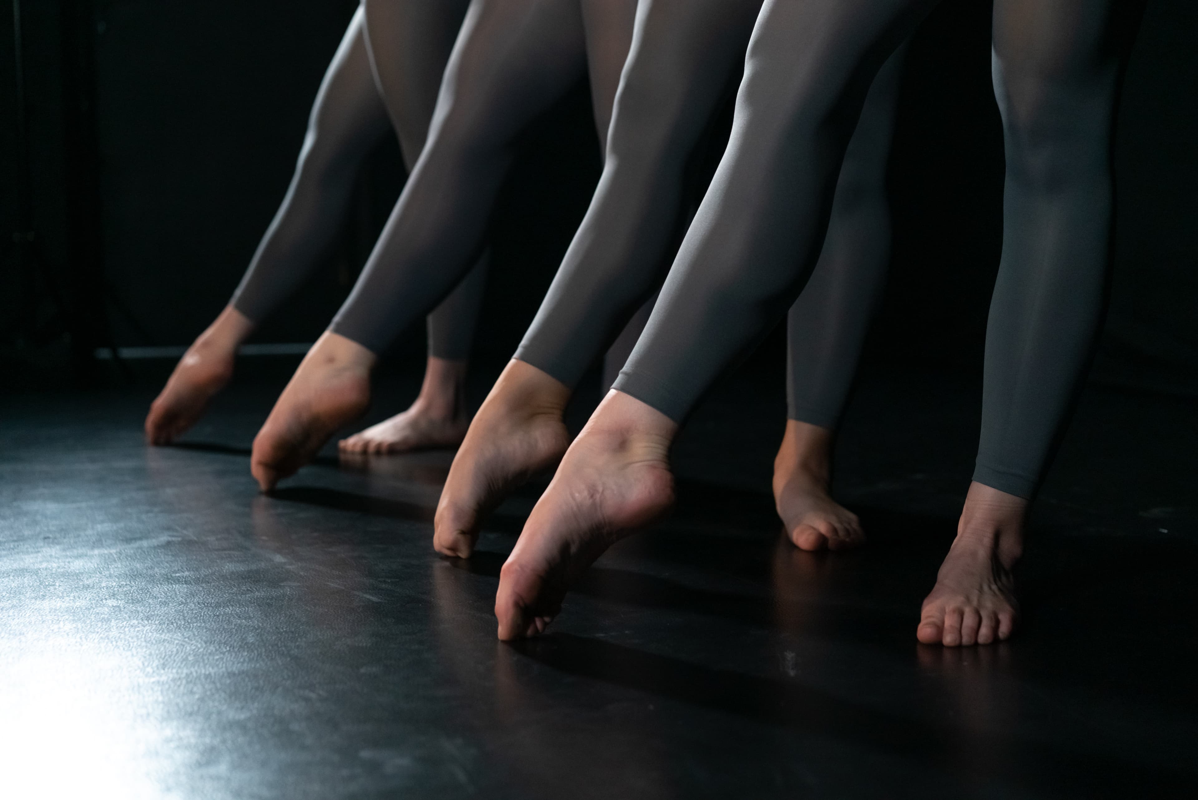 Four dancers stand in a diagonal line performing a toe point in ballet style.