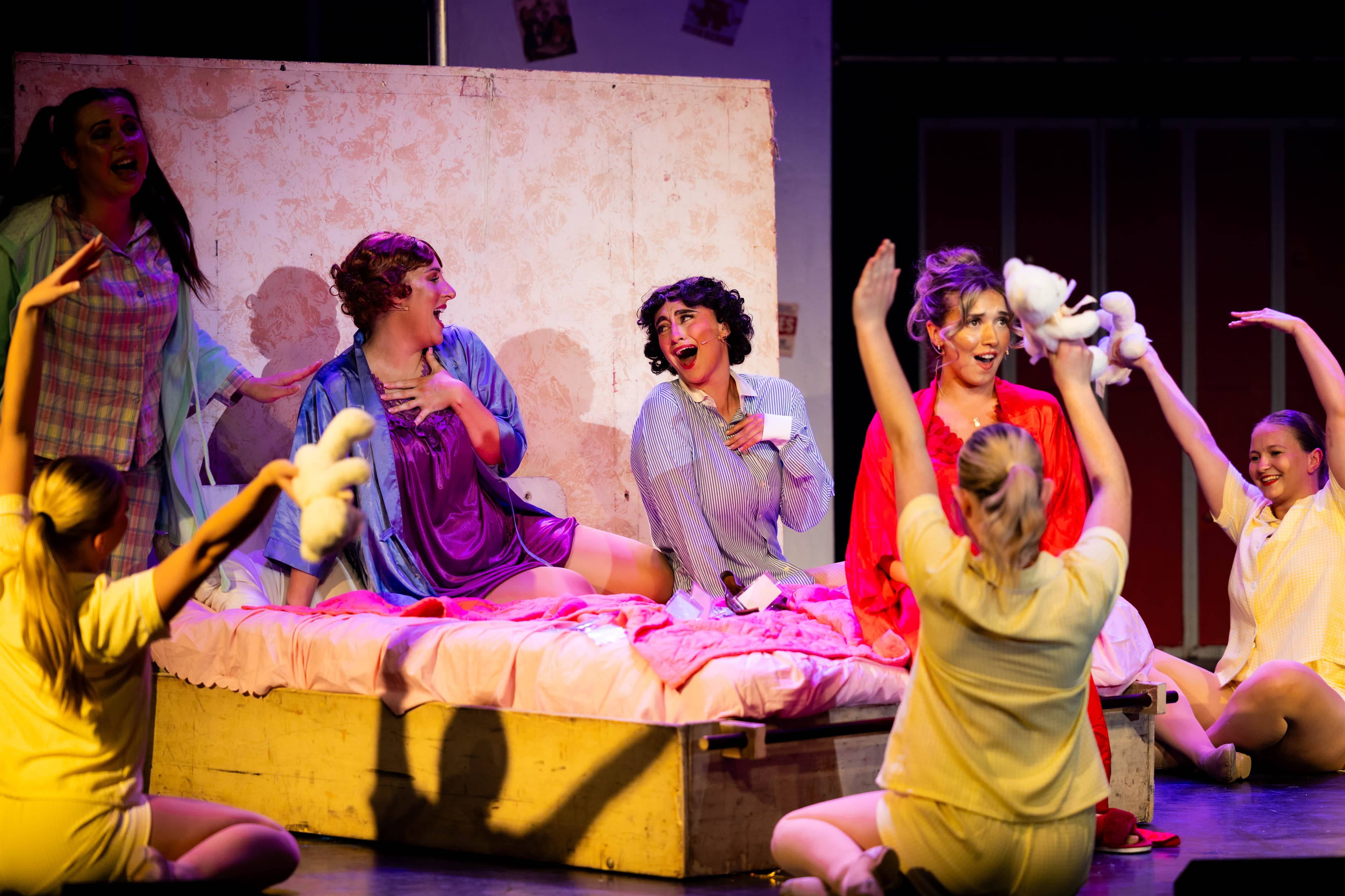The Pink Ladies sit in their pyjamas on a bed singing. The principal dancers dance around them on the floor.