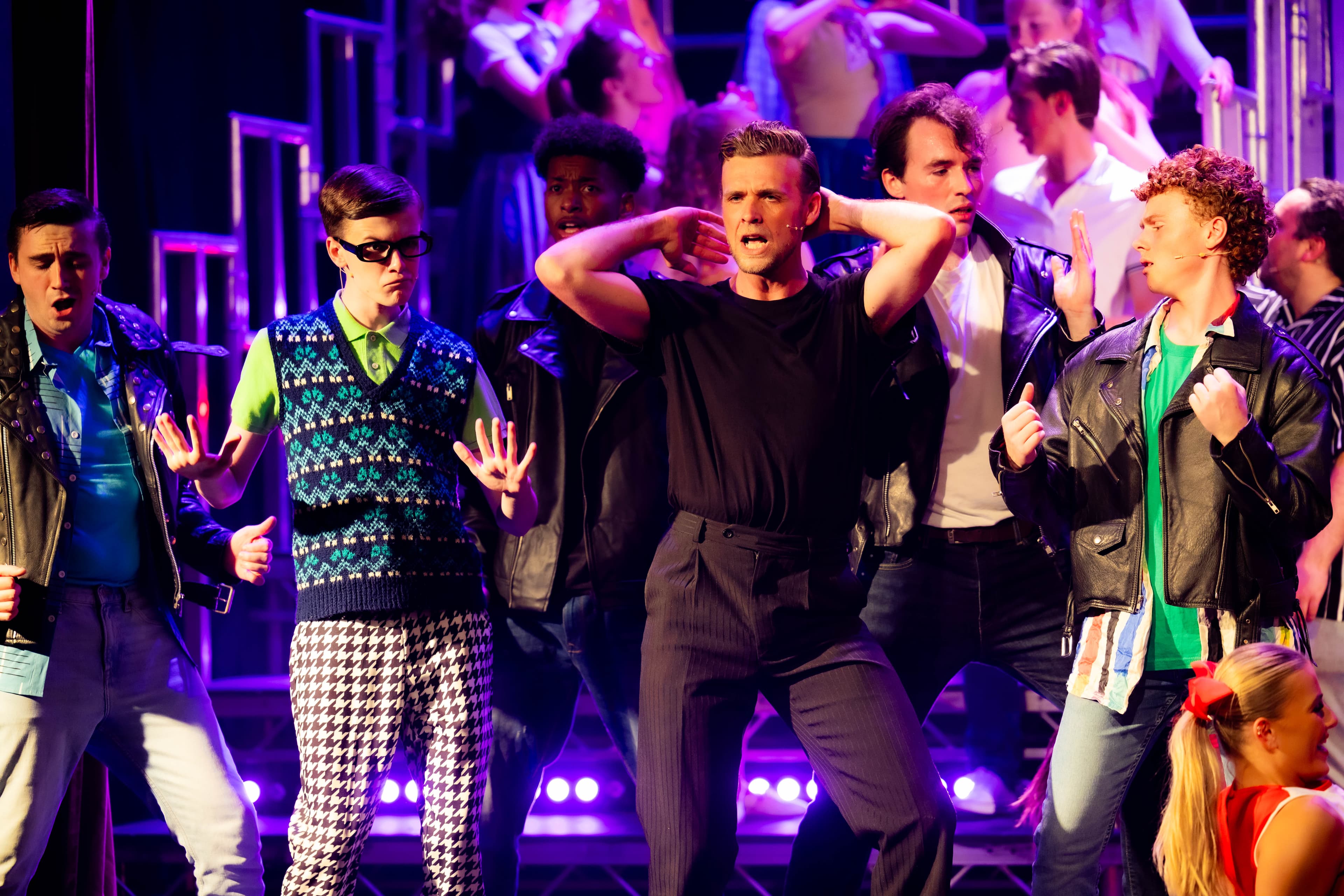 Danny Zuko dances next to Eugene during a song. The rest of the cast dance around them.