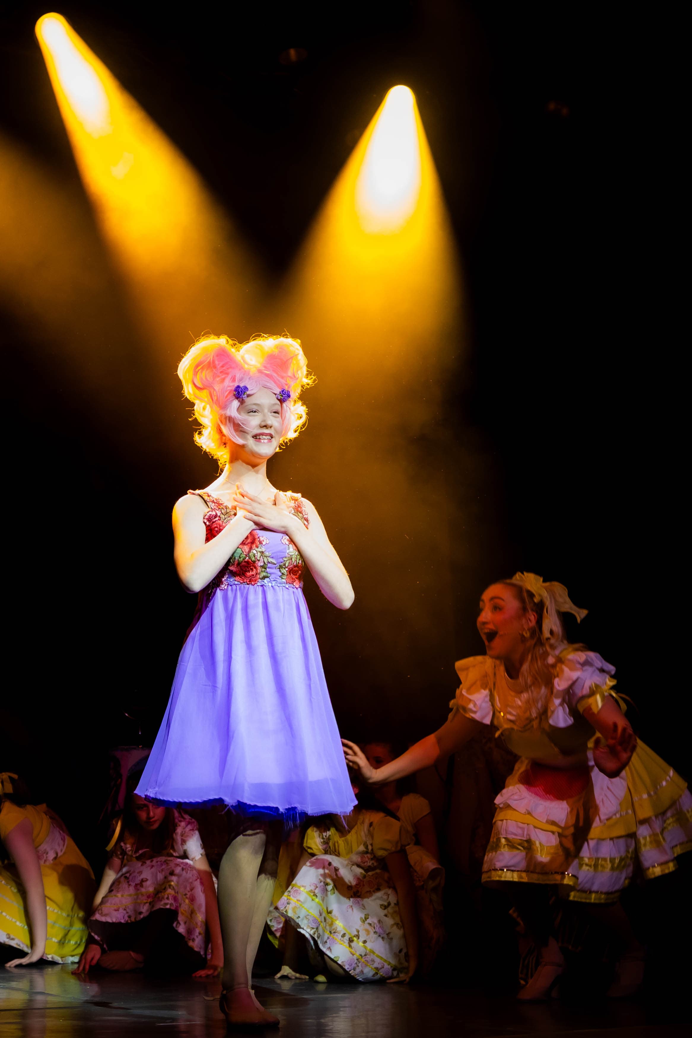 Trixie the Pixies poses while singing a solo, backlit by bright yellow spotlights.