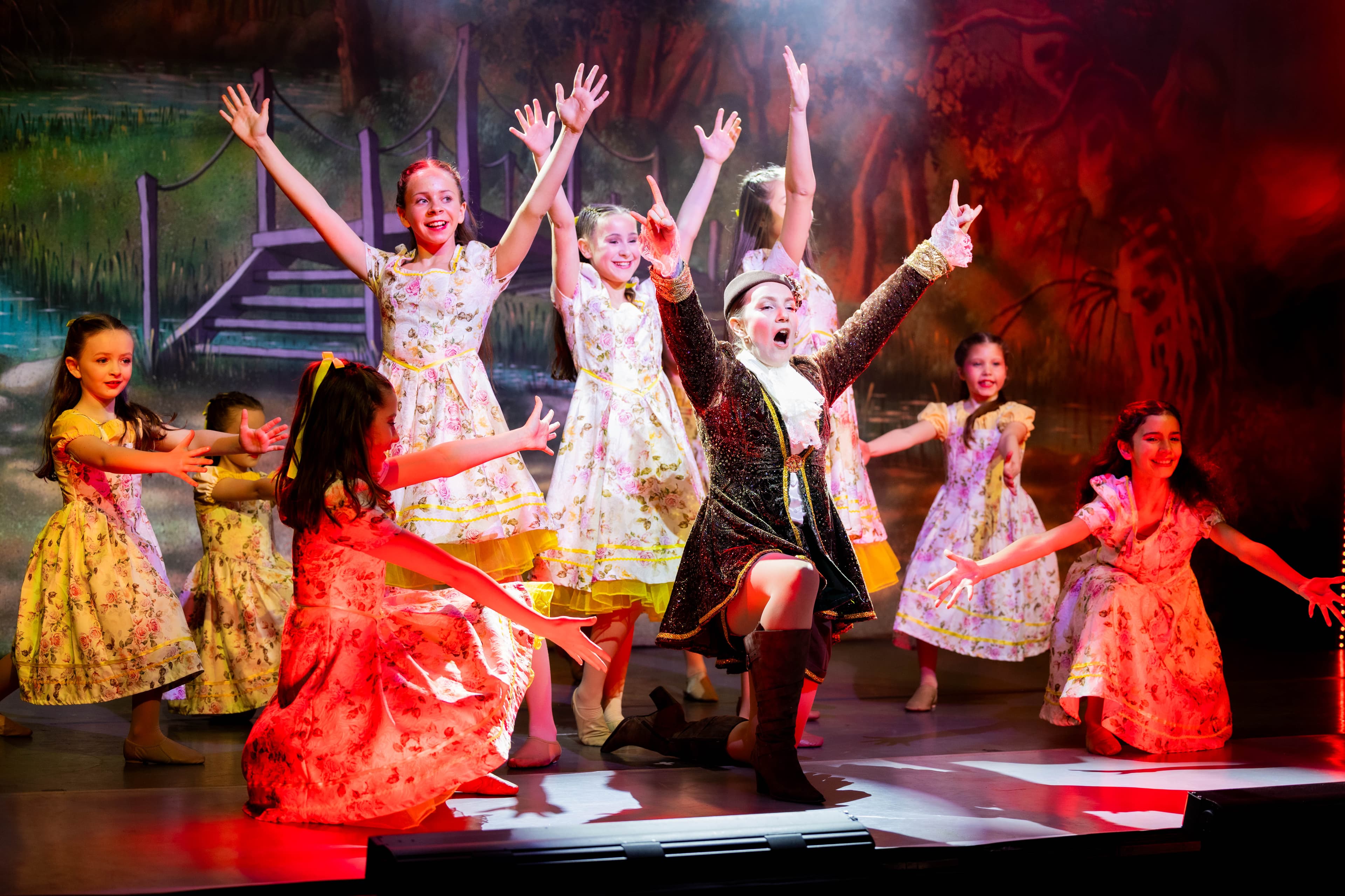 Jack poses knelt on the floor with an arm pointing into the air at the end of a song. He is surrounded by the child cast also posing.
