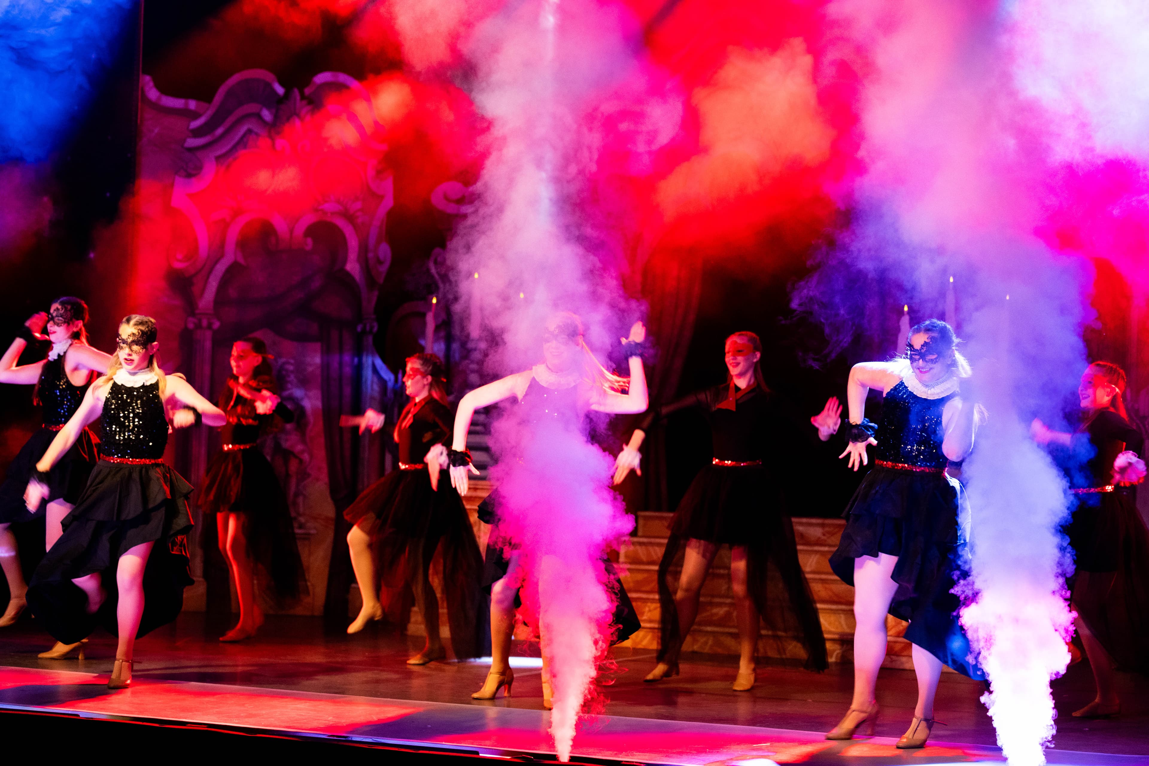 Smoke cannons fire while the cast of Cinderella dance behind during the Masquerade ball. The stage is lit in red and blue.