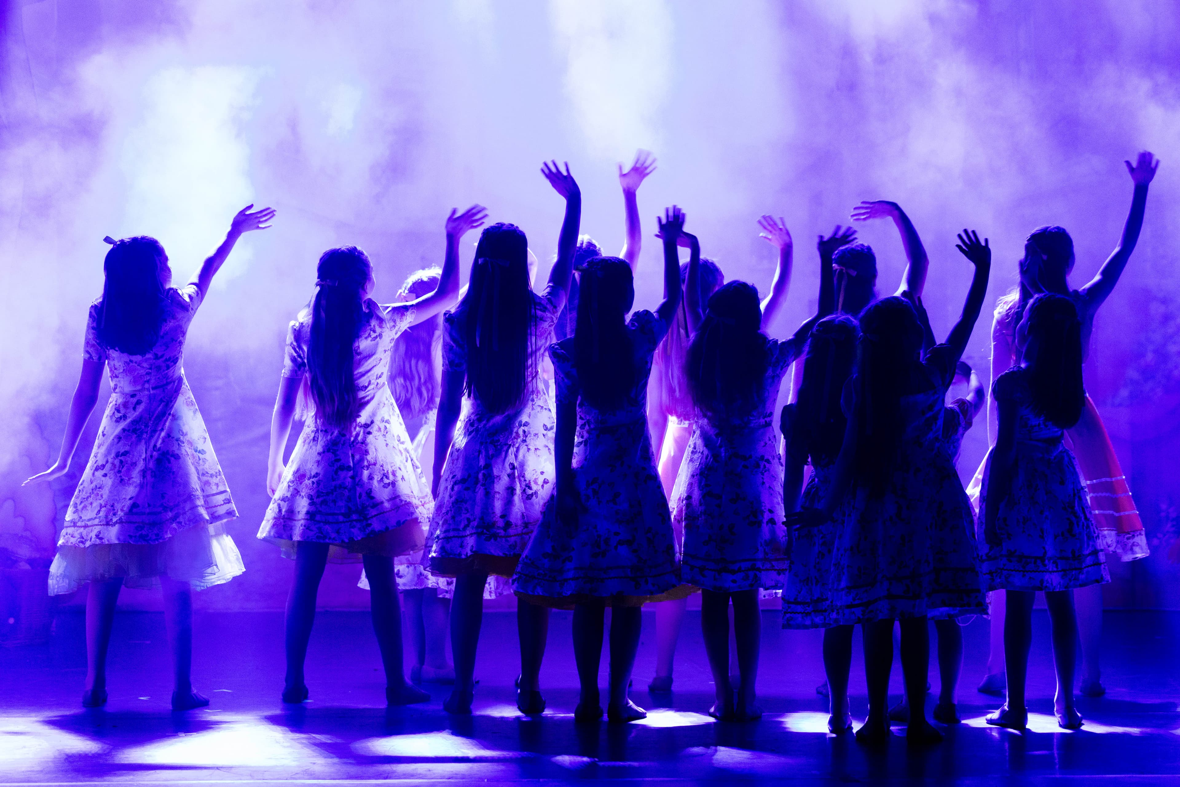 The child cast of Rapunzel are seen silhouetted on a smoky, dark stage. They are waving into the distance.