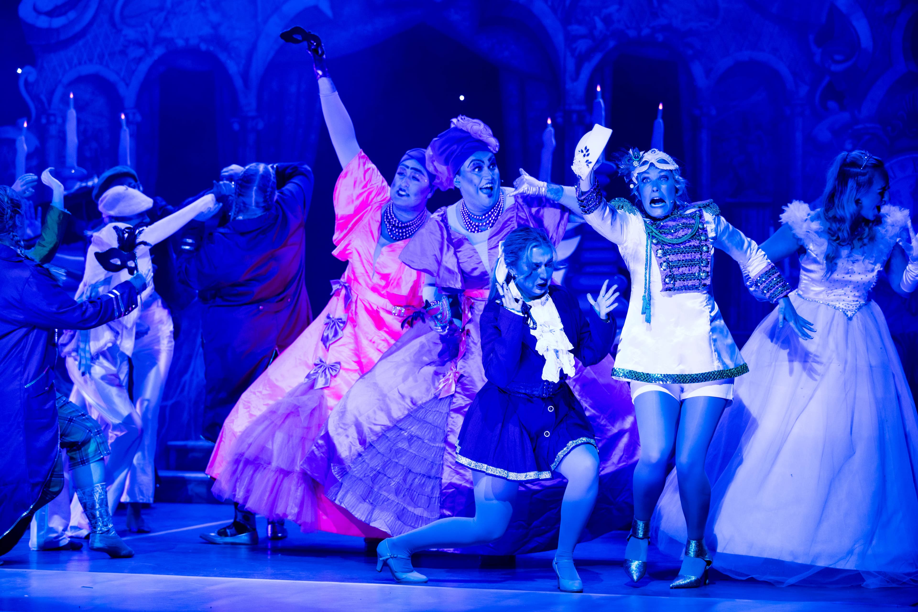 The cast are shown looking scared during the masquerade ball. The stage is lit starkly in just blue.