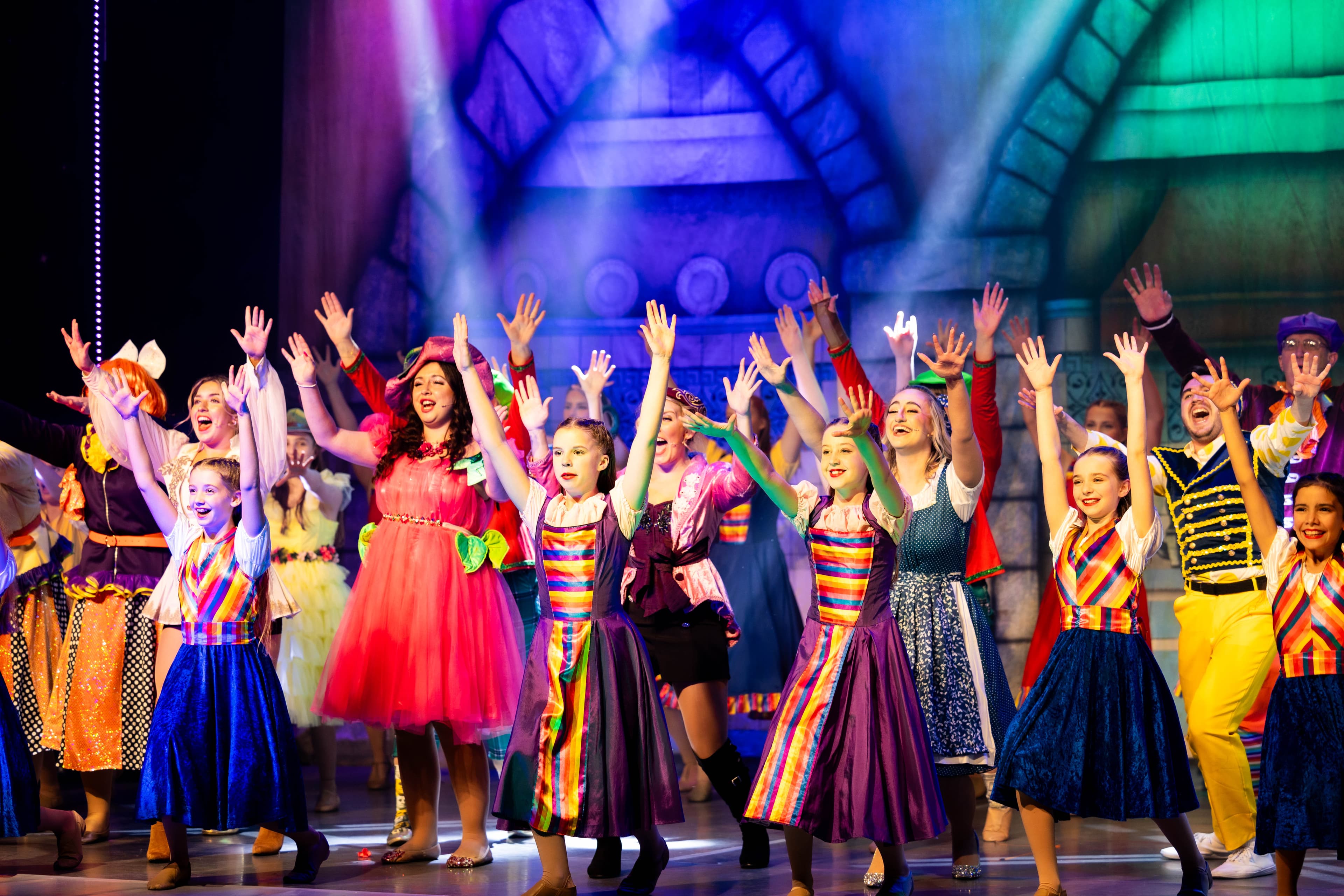 The child cast of Cinderella pose with their arms in the air during a song. The adult cast also pose behind them.