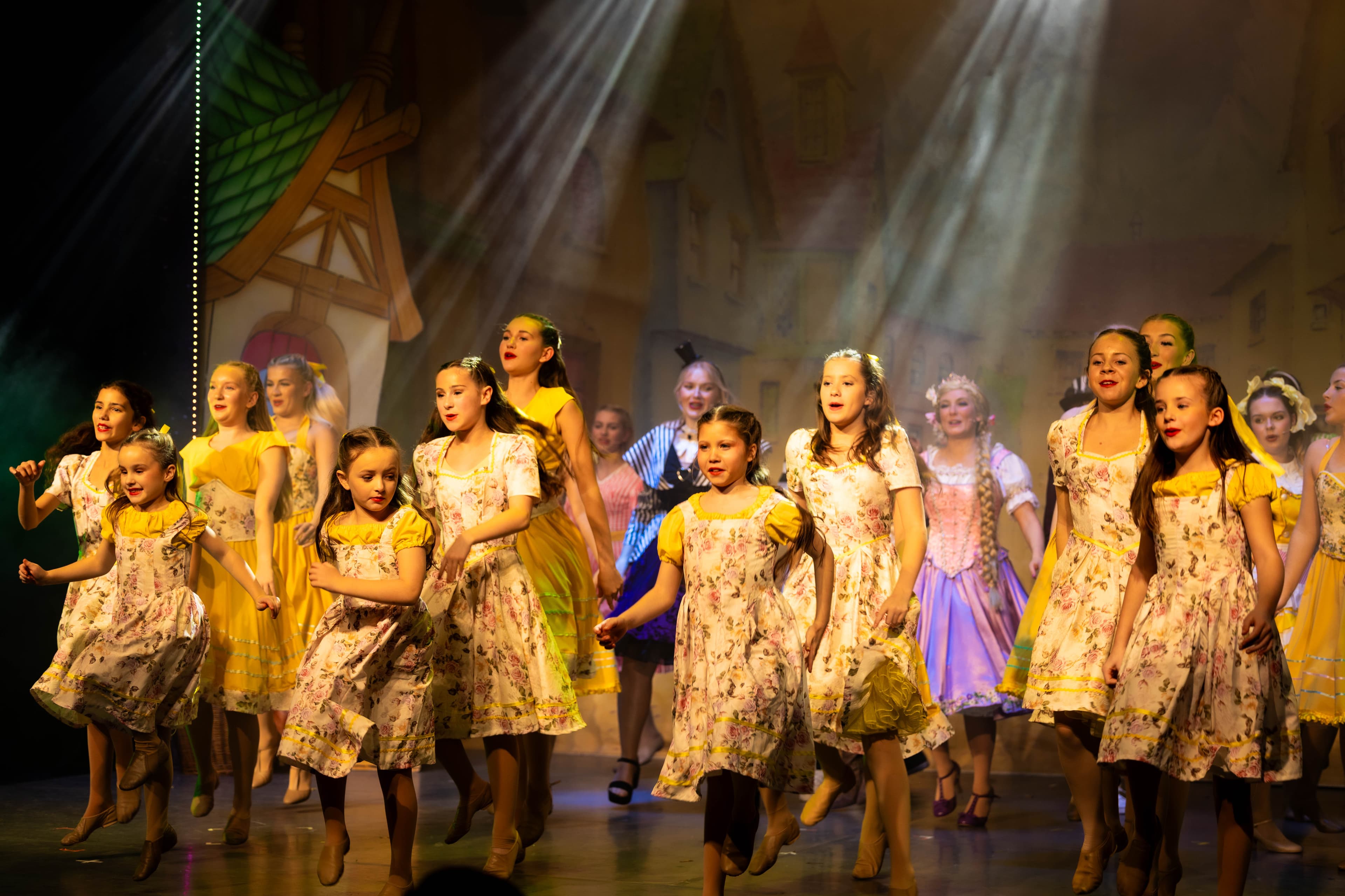 The child cast Rapunzel sing and dance at the front of the stage. The principals can be seen dancing behind.